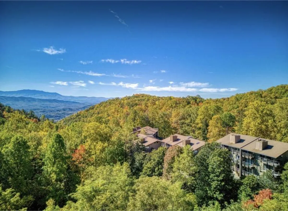 A sweeping view of the mountain range and lush surrounding greenery, with the modern architecture of the property subtly visible. The expansive sky and distant peaks evoke a sense of openness and natural beauty, ideal for romantic exploration and relaxation.