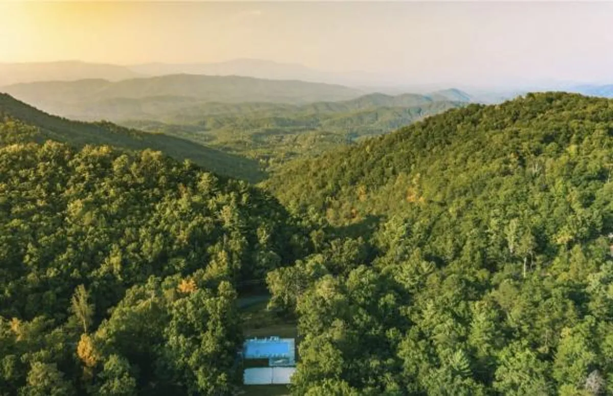 A scenic view combining a sparkling swimming pool with a backdrop of lush greenery and distant mountains, all beneath an open sky. The inviting setting seamlessly merges leisure amenities with the beauty of the outdoors.