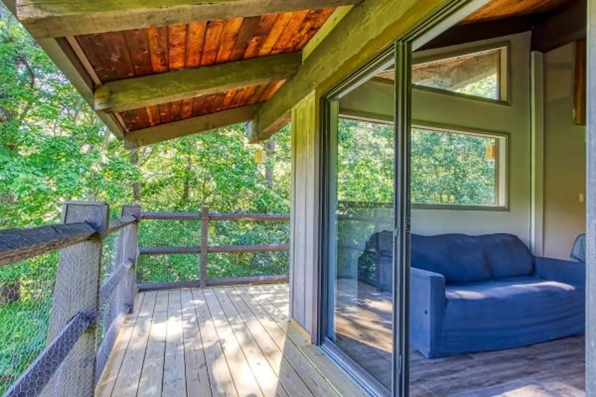 A serene interior shot showing a soft, inviting sofa positioned by expansive windows that open to the deck area. The windows frame lush, green views, and the tranquil ambiance suggests a perfect spot for unwinding and enjoying the scenery.