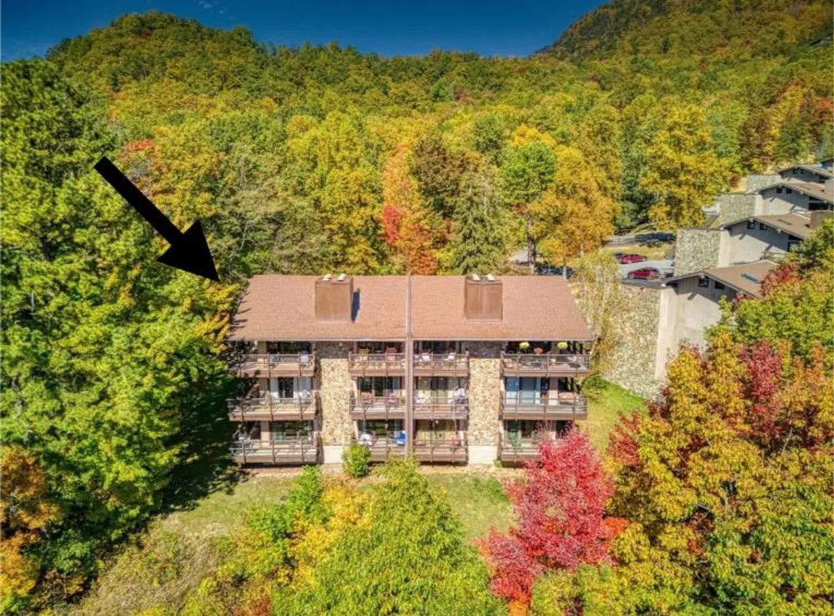 The image showcases a multi-story condo building nestled among towering trees with vibrant, colorful fall foliage. The setting is peaceful and inviting, giving a sense of seclusion and natural beauty. The building’s exterior is warm and welcoming, surrounded by the serene landscape of the Smoky Mountains.