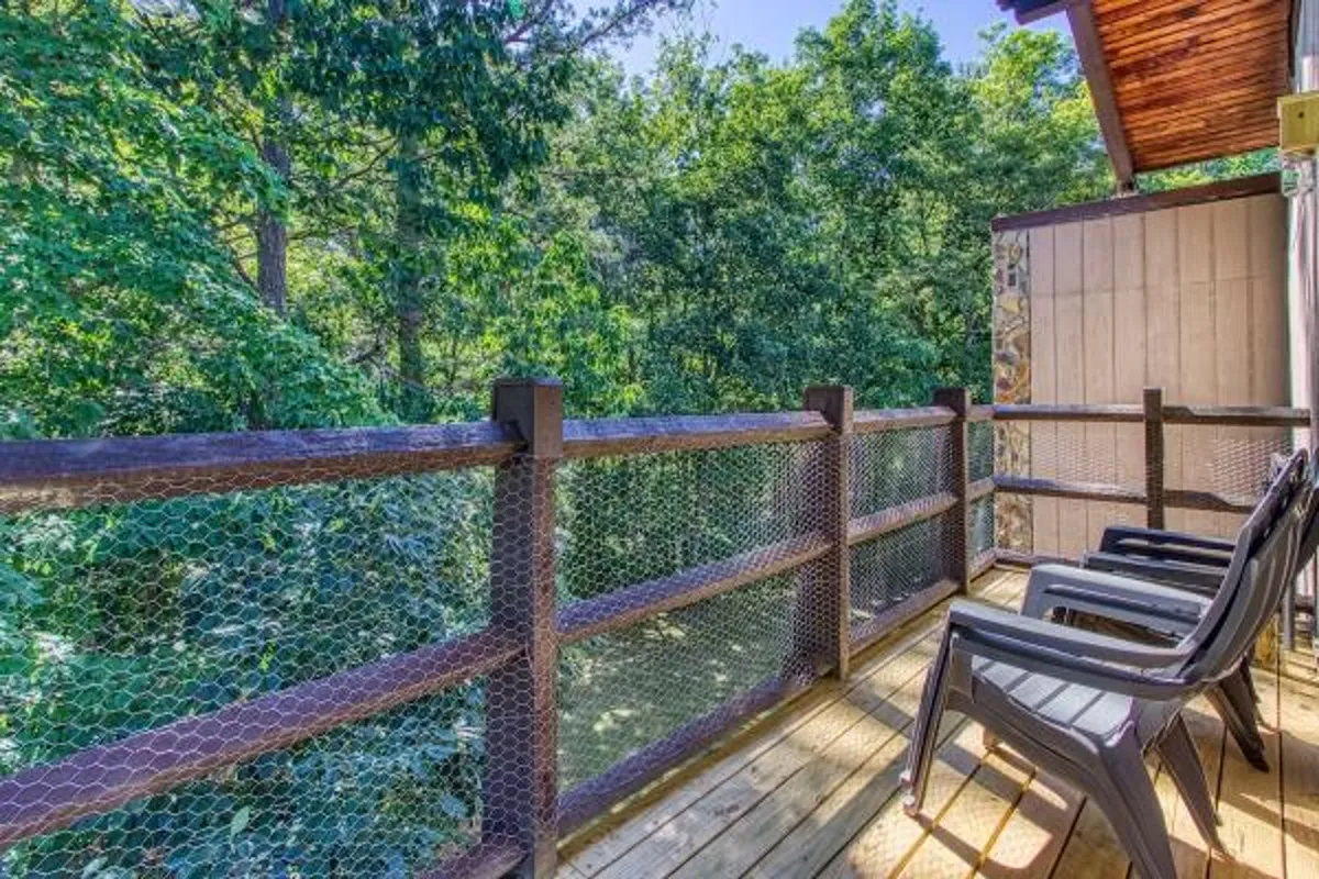 A peaceful wooden deck adorned with comfortable chairs, bordered by a classic wooden railing and surrounded by tall trees. The space feels private and immersed in nature, ideal for enjoying fresh mountain air or a quiet evening of stargazing.