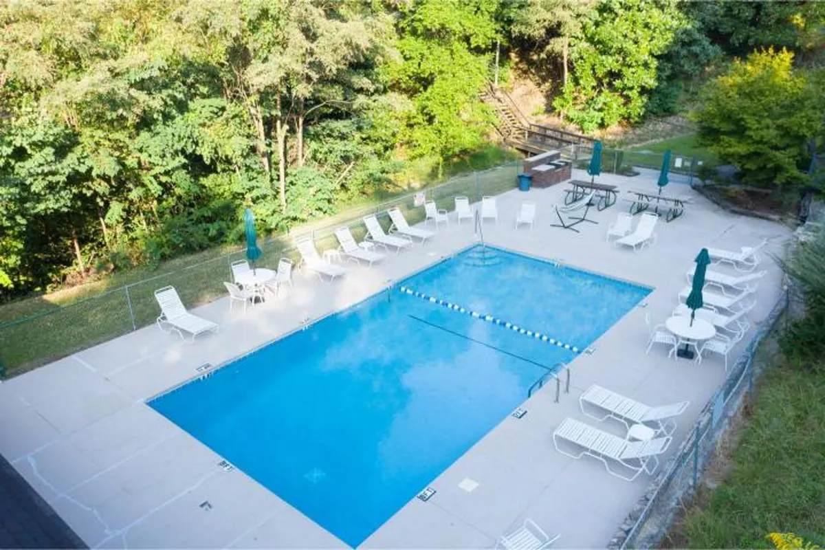 A sun-drenched swimming pool is surrounded by lounge chairs and lush greenery. There's a picnic table nearby, hinting at spaces for family gatherings and outdoor meals. The overall scene is welcoming and designed for fun, safe, and easy relaxation just steps from the condo.
