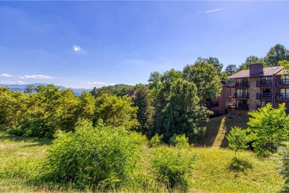 A serene exterior shot of the condo-cabin nestled among lush greenery, with distant mountain views and a private balcony visible. The early morning light highlights the peaceful setting, inviting guests to relax and connect with nature right outside their door.