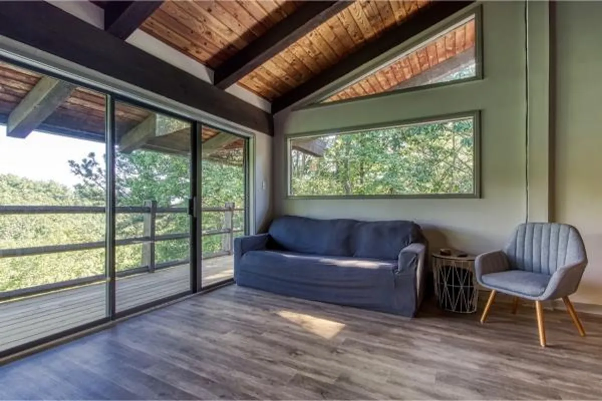 A cozy living room features a soft sofa facing a sliding glass door, with views of trees just outside. The space is bathed in natural light, inviting families to relax after a day outdoors while still feeling connected to the surrounding nature.